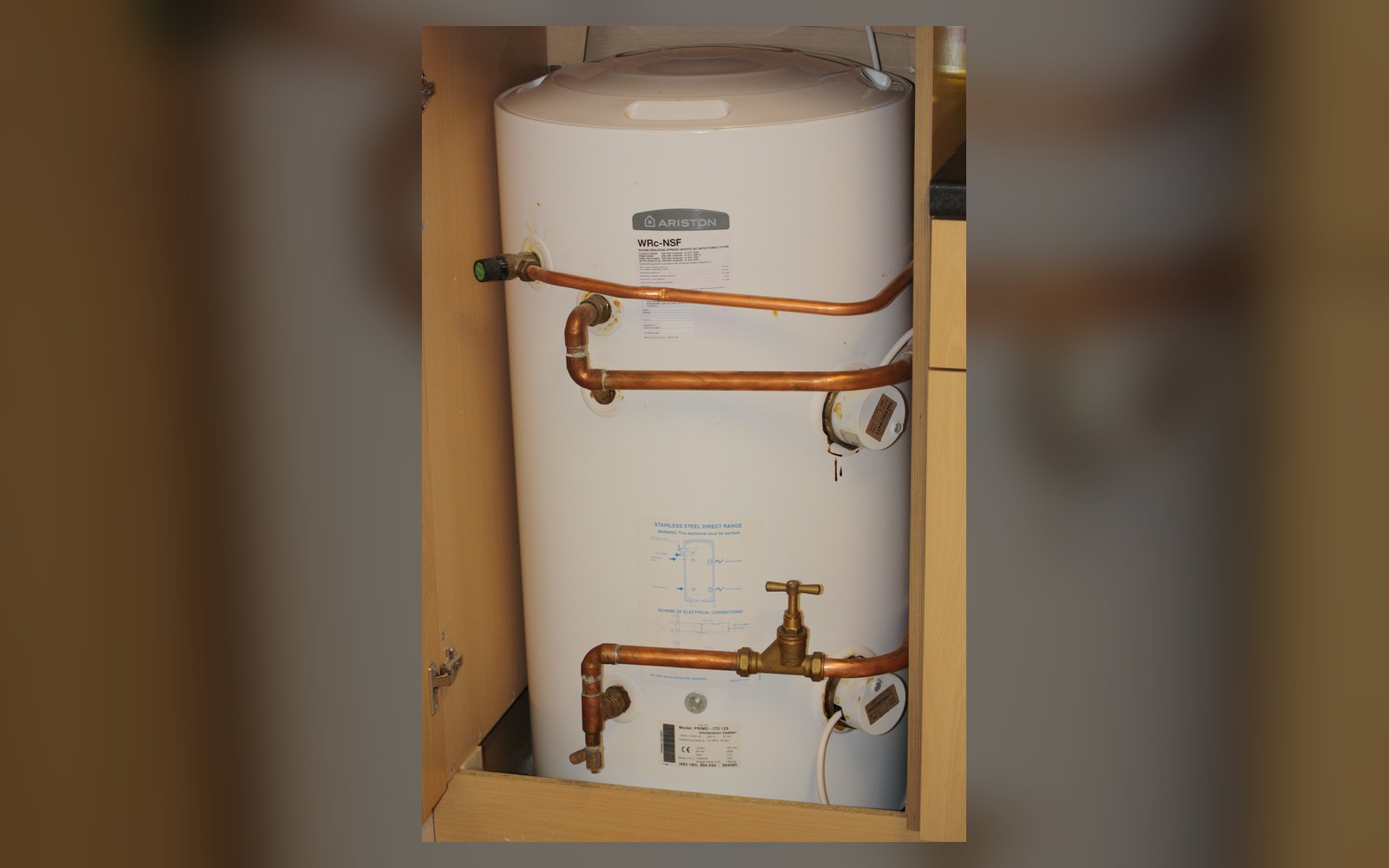 Insulated hot-water cylinder with connected pipes in a residential utility room